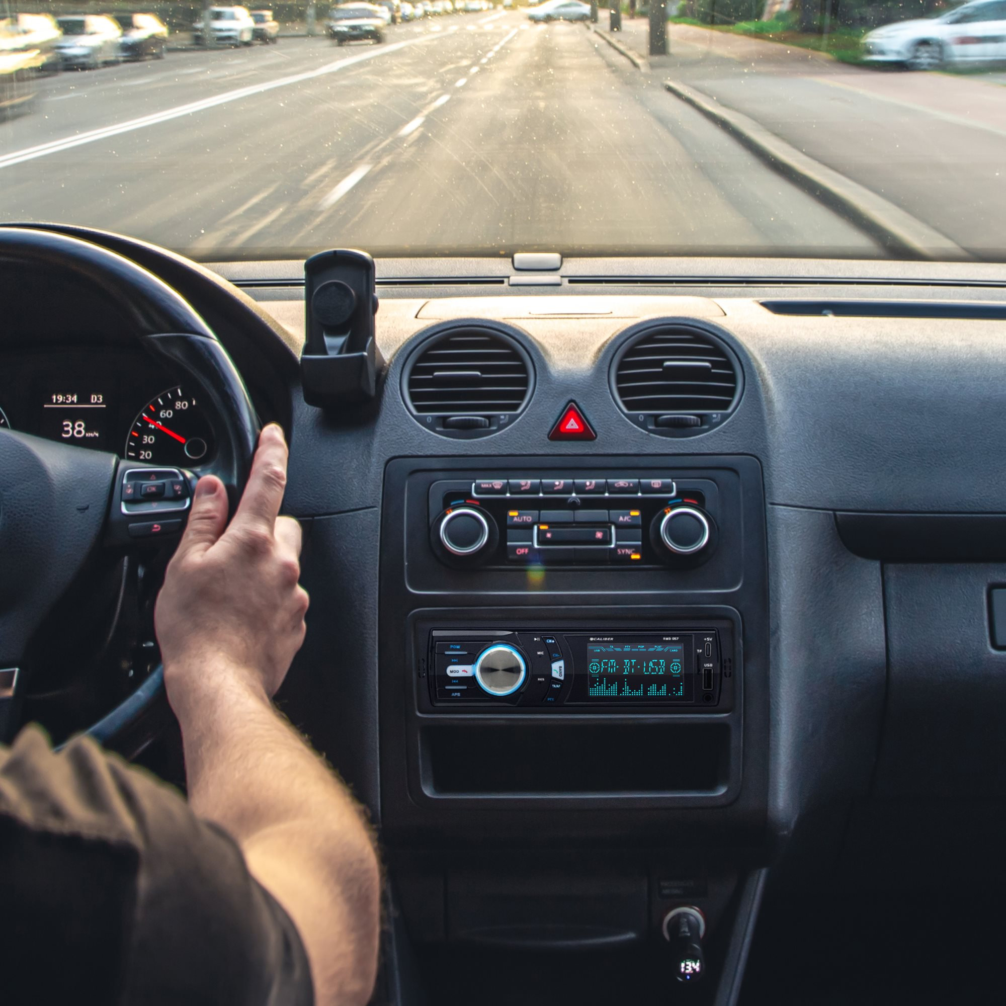 Interior view of a car dashboard with a hand on the steering wheel.