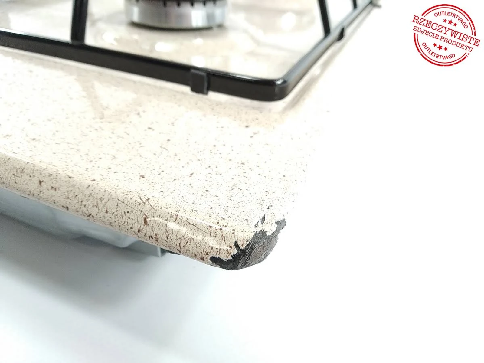 Narożnik blatu kuchennego z palnikiem gazowym i widoczną uszkodzoną krawędzią.