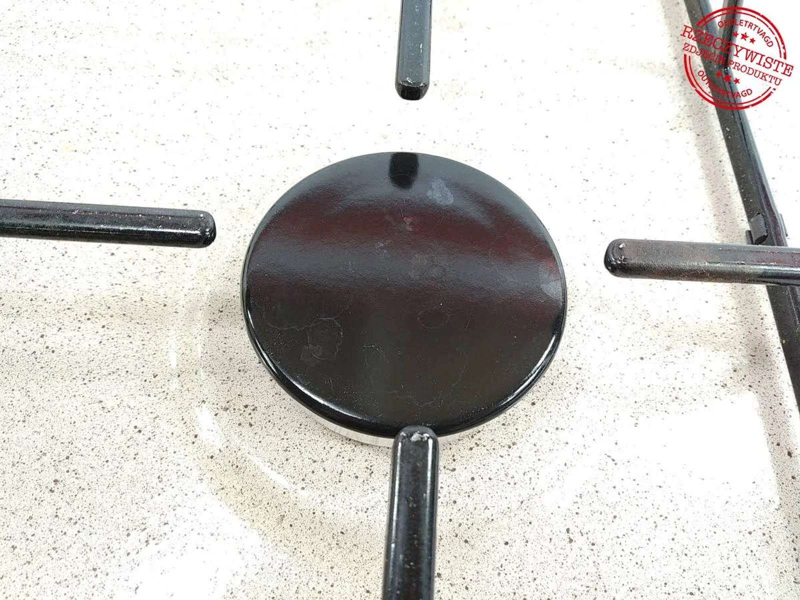 Czarny palnik kuchenki z czarną kratką na jasnej powierzchni.