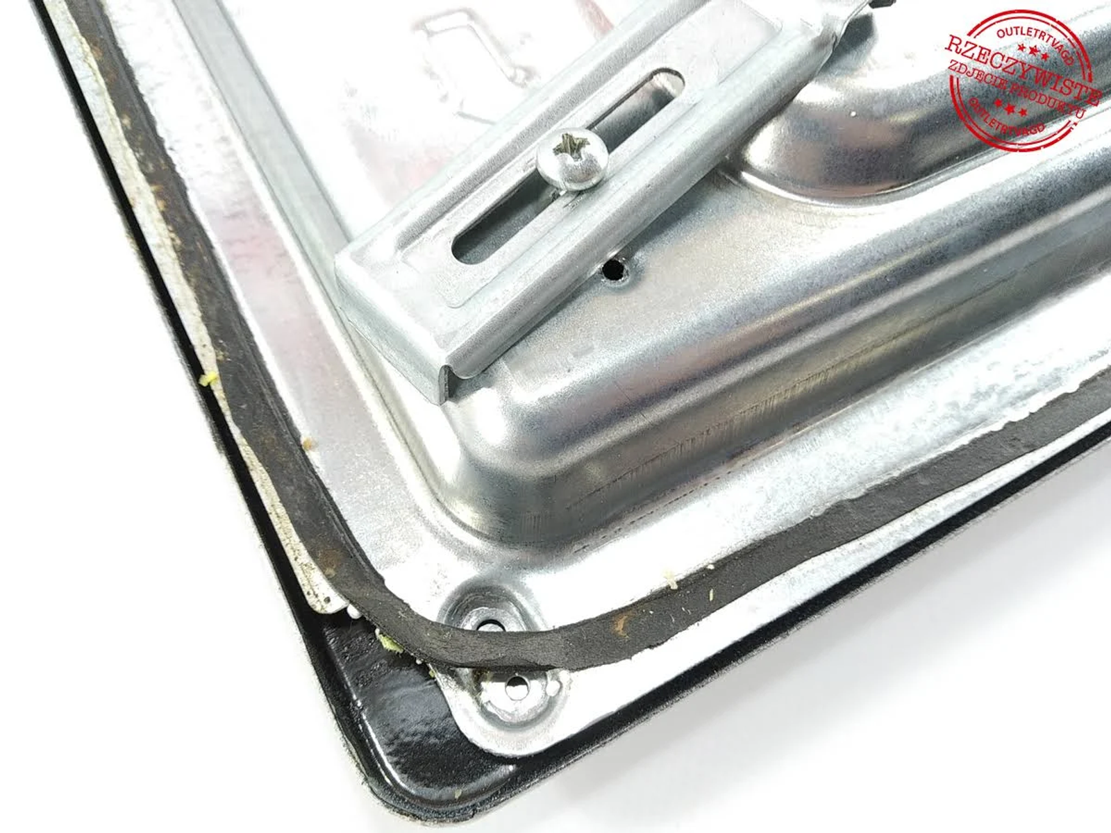 Zbliżenie metalowego elementu piekarnika ze śrubą i czarną uszczelką gumową. Białe tło.