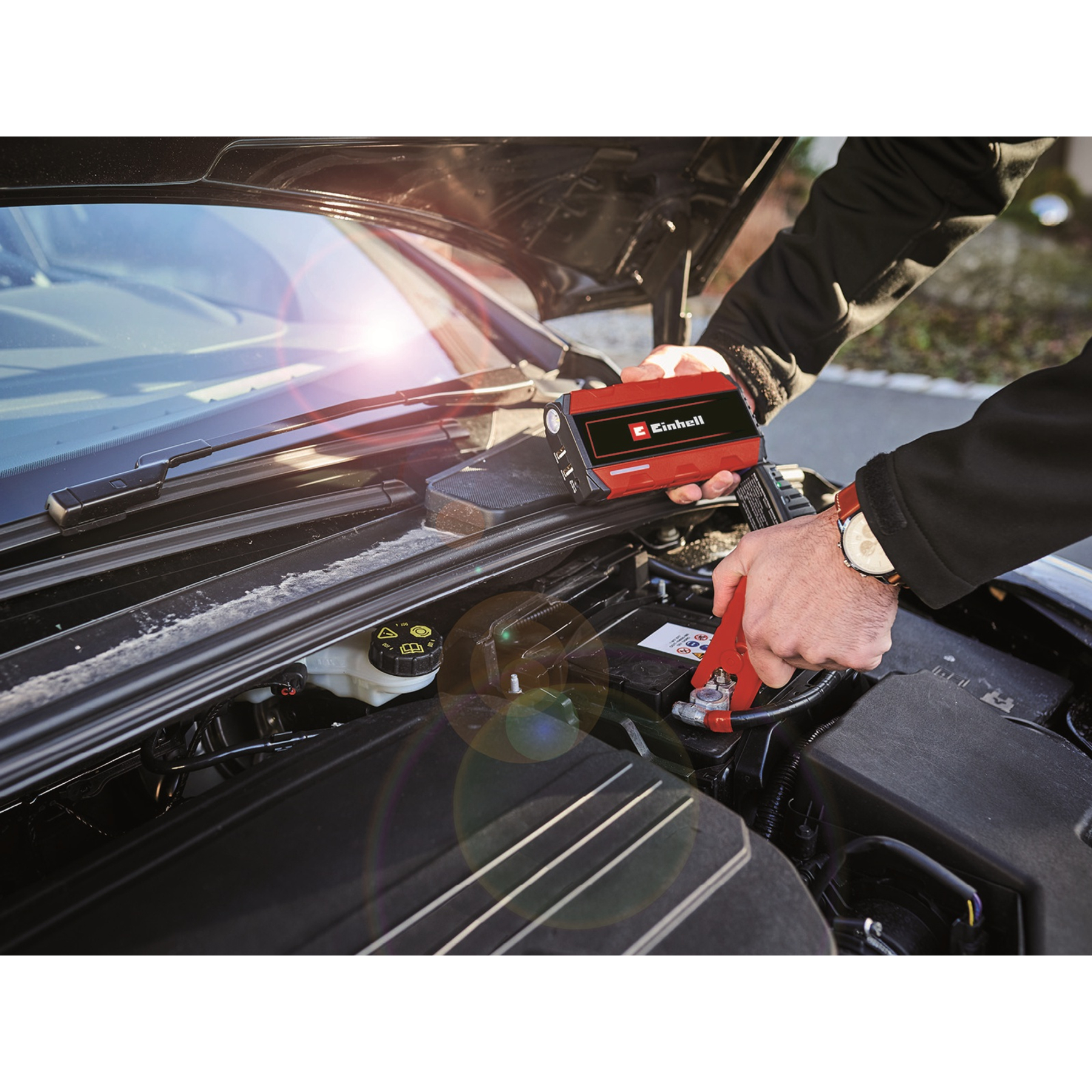 Hände schließen ein rotes und schwarzes Starthilfegerät an eine Autobatterie an.