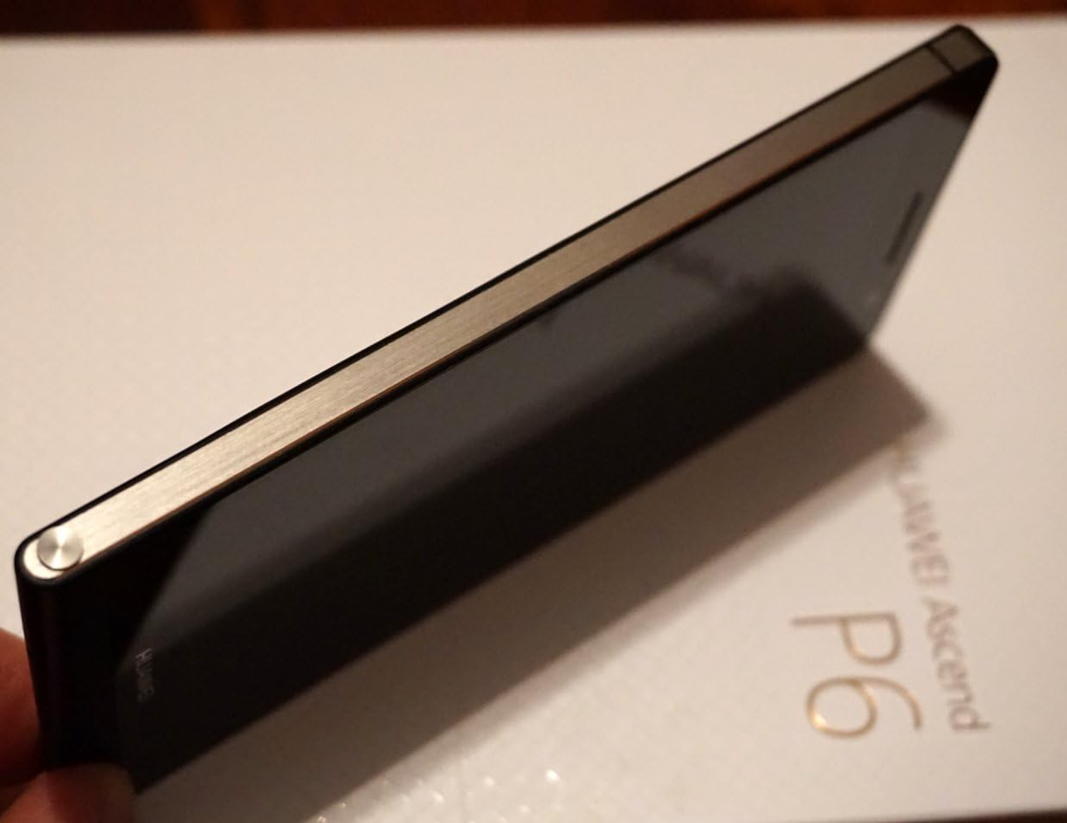 Schwarzes Smartphone mit silbernem Rand, auf einer weißen Box liegend, Huawei Ascend P6 Logo.