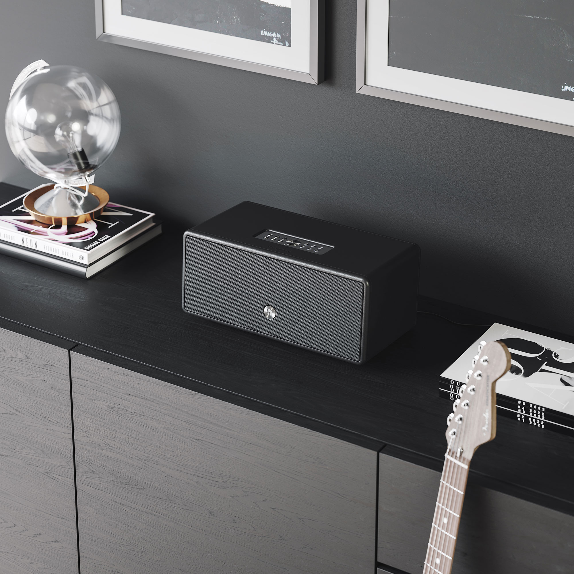 Black speaker on a black cabinet, with books and a globe, in a room with dark walls.
