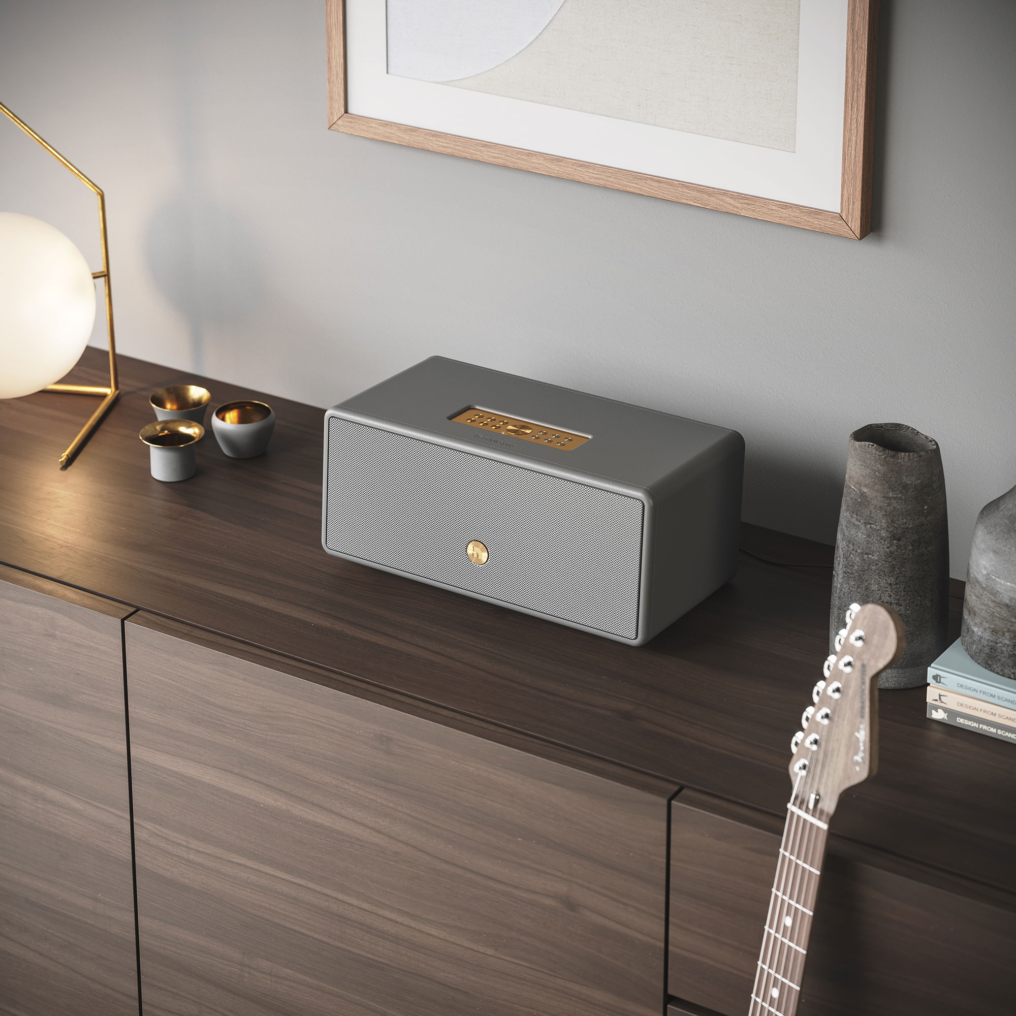 A gray speaker on a wooden cabinet with a guitar and other decorations.