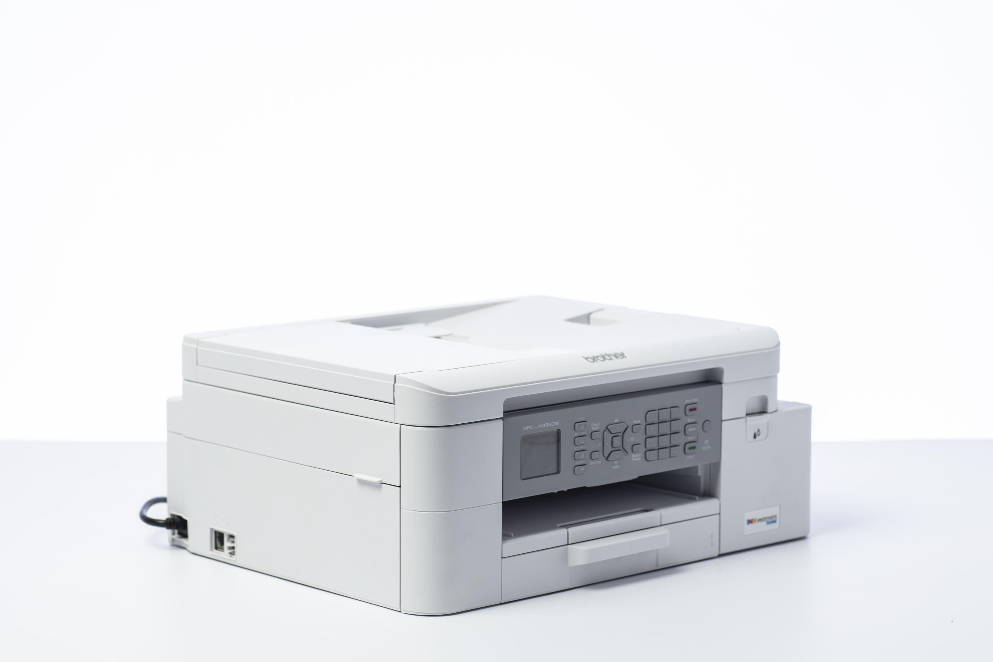 Biała drukarka na białej powierzchni z białym tłem. Drukarka ma markę "Brother".