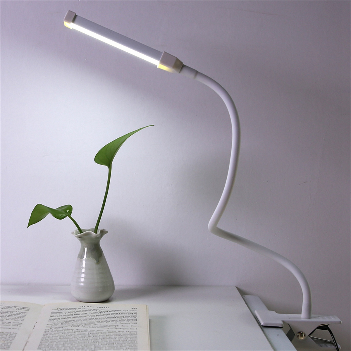 Weiße Schreibtischlampe mit flexiblem Hals und kleiner Vase mit grünen Blättern.