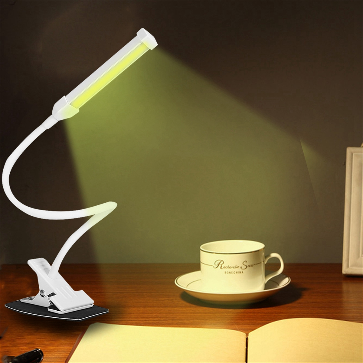 Schwanenhals-Schreibtischlampe, die auf ein Buch und eine Tasse scheint. Der Hintergrund ist dunkel.