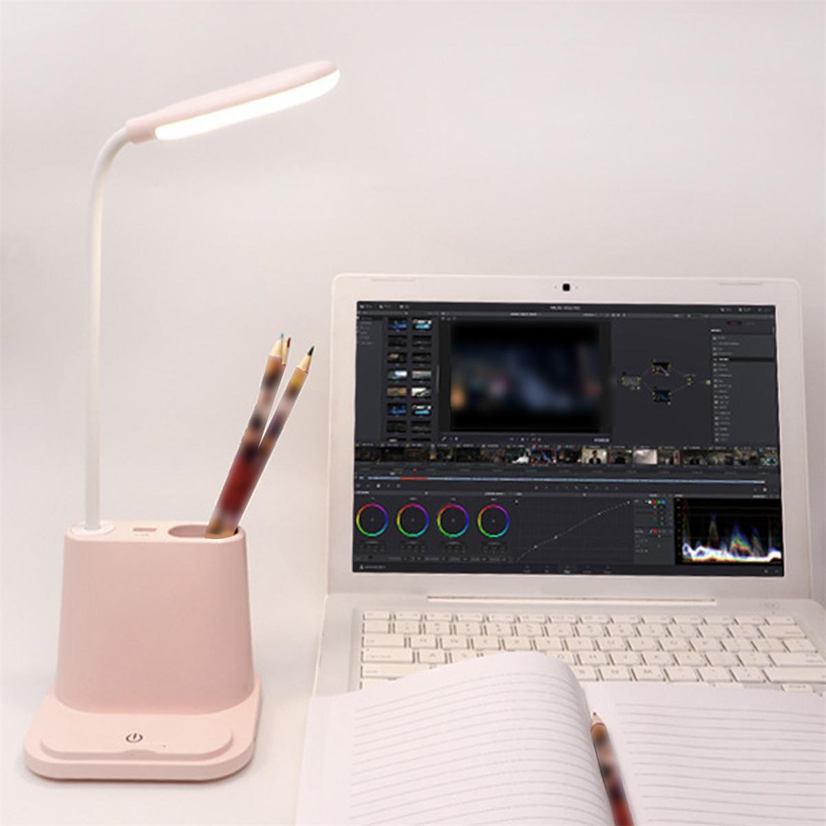 Eine rosa Schreibtischlampe mit Stifthalter, Stiften, einem Laptop und einem Notizbuch.
