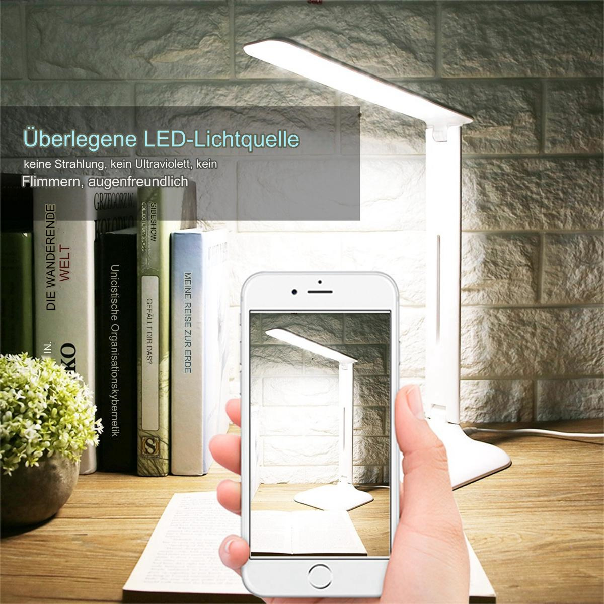 Eine Hand, die ein Telefon hält, auf dem eine weiße Schreibtischlampe abgebildet ist. Bücher und eine Pflanze sind im Hintergrund.