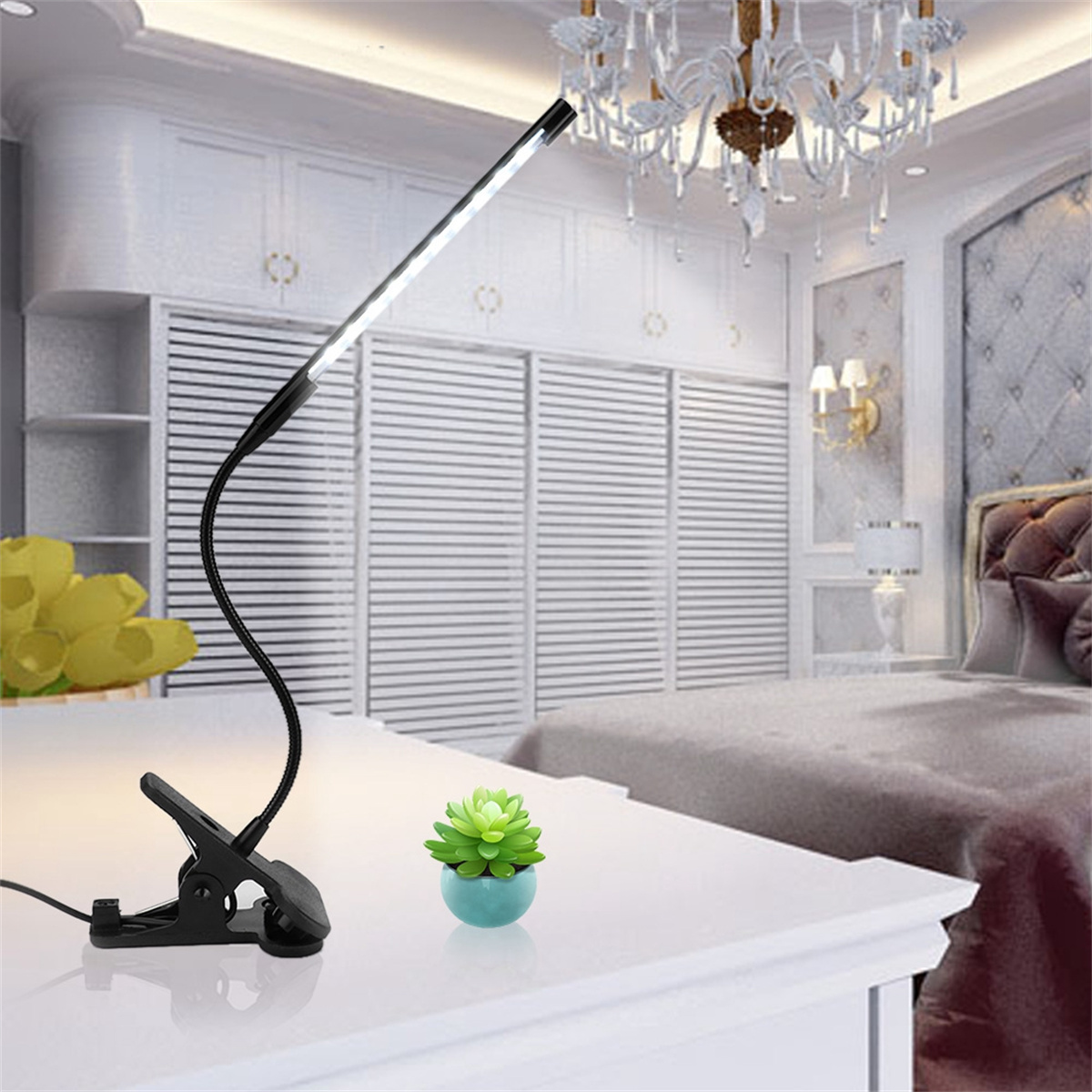 Schwarze Schreibtischlampe mit flexiblem Hals, auf weißem Tisch. Grüne Pflanze daneben.