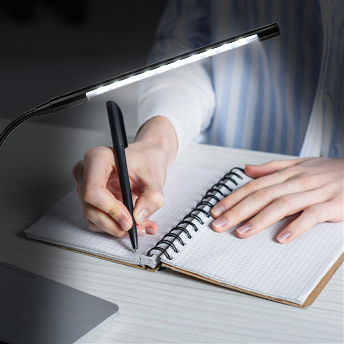 Person schreibt in einem Notizbuch unter einer schwarzen LED-Schreibtischlampe. Dunkler Hintergrund, fokussiertes Licht.