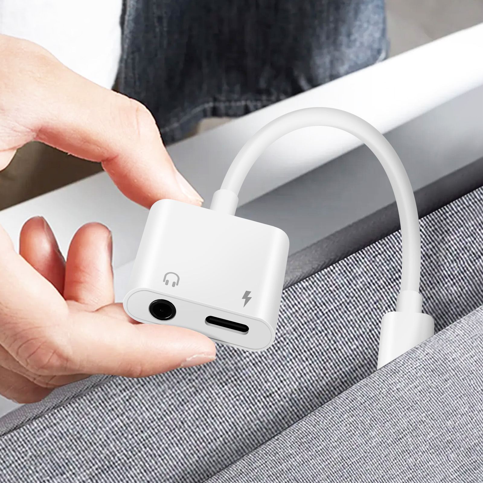 Una mano che tiene un adattatore bianco con porte per cuffie e ricarica.