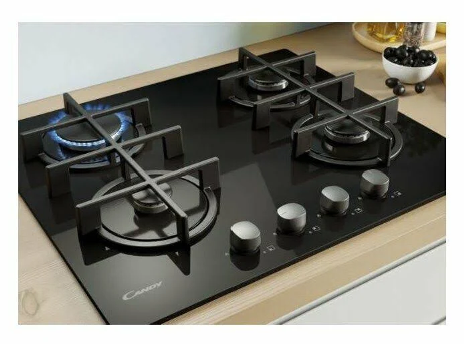 Czarna płyta grzejna z czterema palnikami i pokrętłami sterowania. Płyta grzejna znajduje się na jasnej powierzchni.