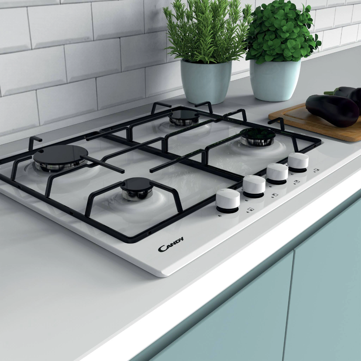 Biała kuchenka gazowa z czarnymi kratkami. Dwie rośliny, deska do krojenia z bakłażanami w tle.