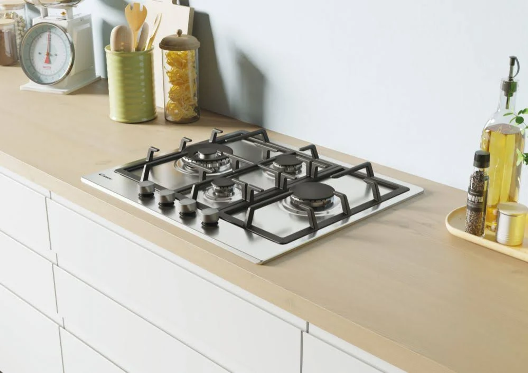 Nowoczesna kuchenka gazowa na jasnym drewnianym blacie, z innymi przedmiotami kuchennymi w tle.
