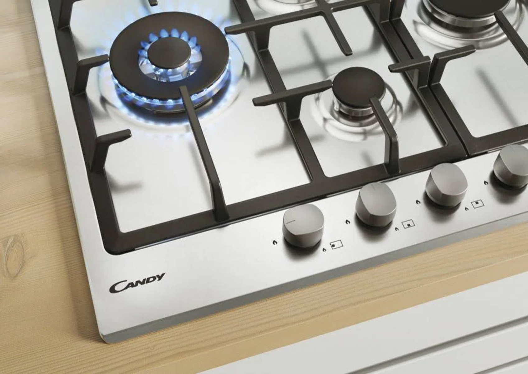 Zbliżenie na kuchenkę gazową ze stali nierdzewnej z niebieskim płomieniem i pokrętłami.