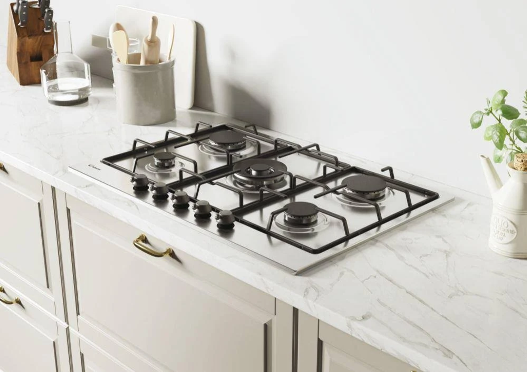 Blat kuchenny z gazową płytą grzejną ze stali nierdzewnej. Obok stoją naczynia i roślina.