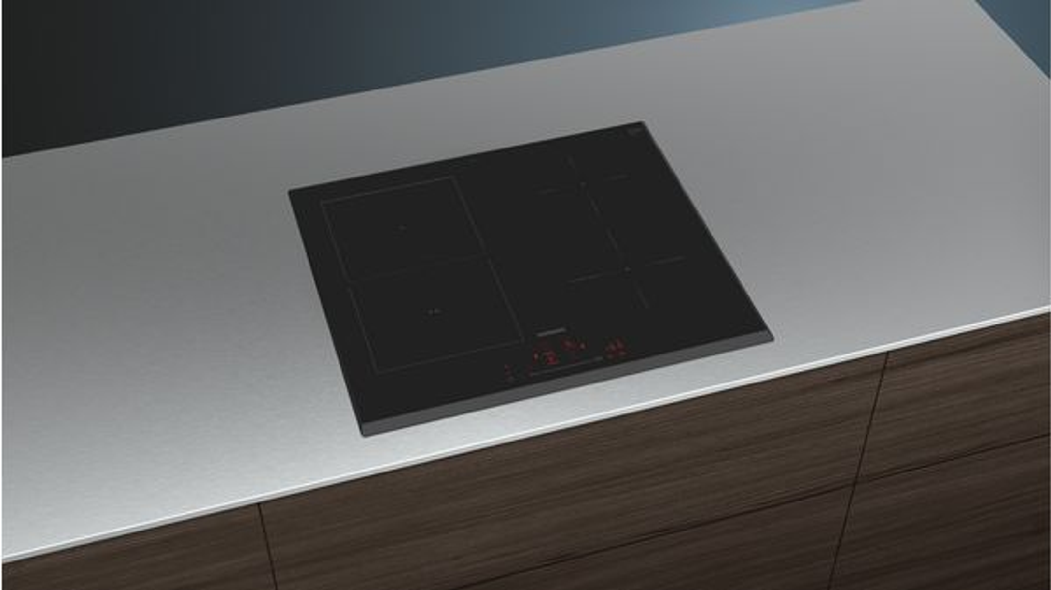 Una encimera gris clara con una placa negra empotrada. Tiene cuatro quemadores y un panel.