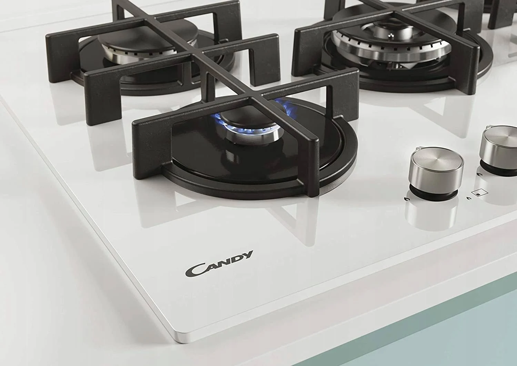 Zbliżenie białej płyty grzewczej z czterema palnikami i czarnymi rusztami.