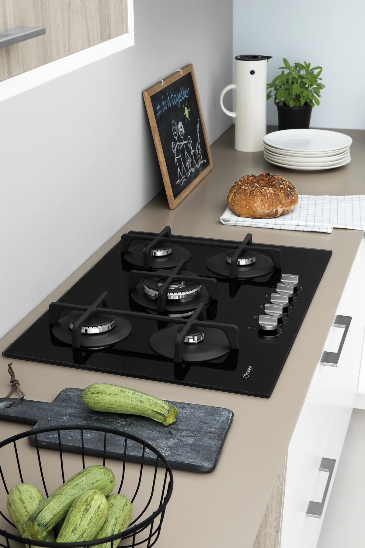 Scena di cucina con piano cottura a gas nero, verdure e utensili da cucina.