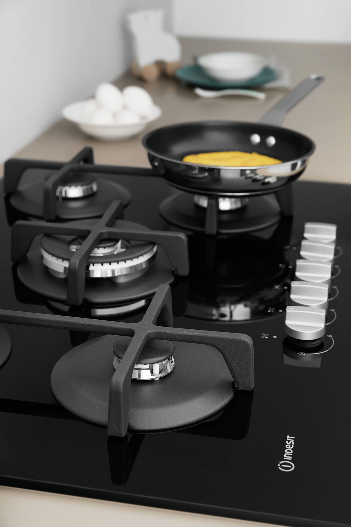 Piano cottura nero con padella, ciotola di uova e manopole. Nero e acciaio inox.