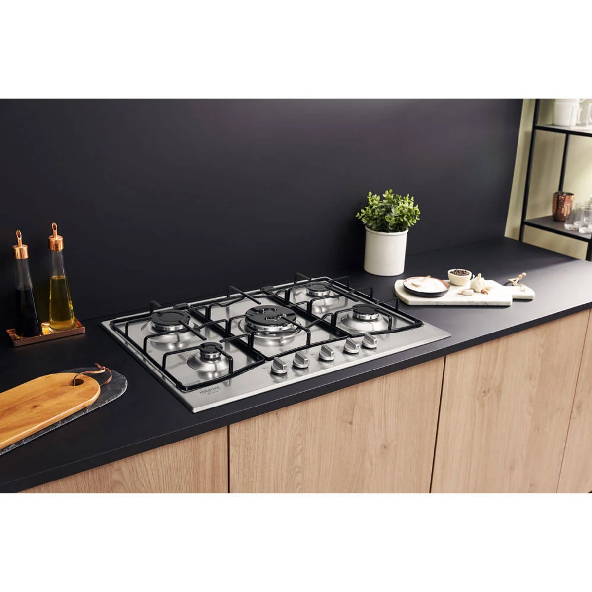 Płyta grzewcza ze stali nierdzewnej z pięcioma palnikami i pokrętłami, na czarnym blacie, scena kuchenna.