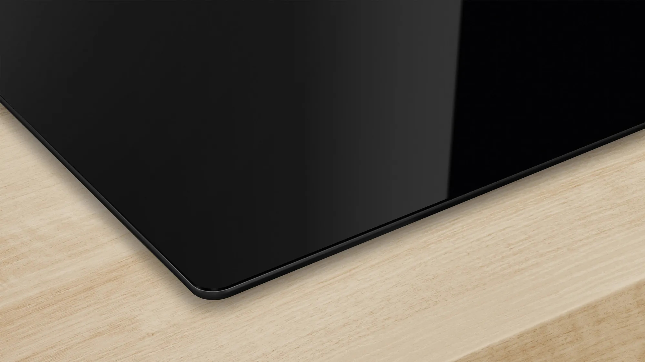 Zbliżenie eleganckiej czarnej płyty grzewczej płynnie zintegrowanej z jasnym drewnianym blatem.