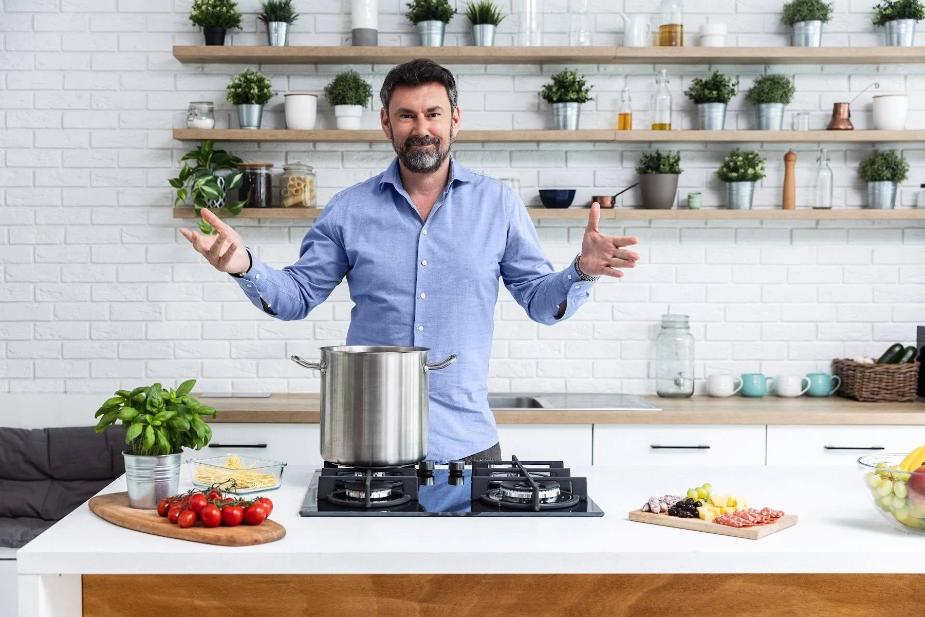 Mężczyzna w niebieskiej koszuli w kuchni, gestykuluje. Garnek na płycie gazowej.