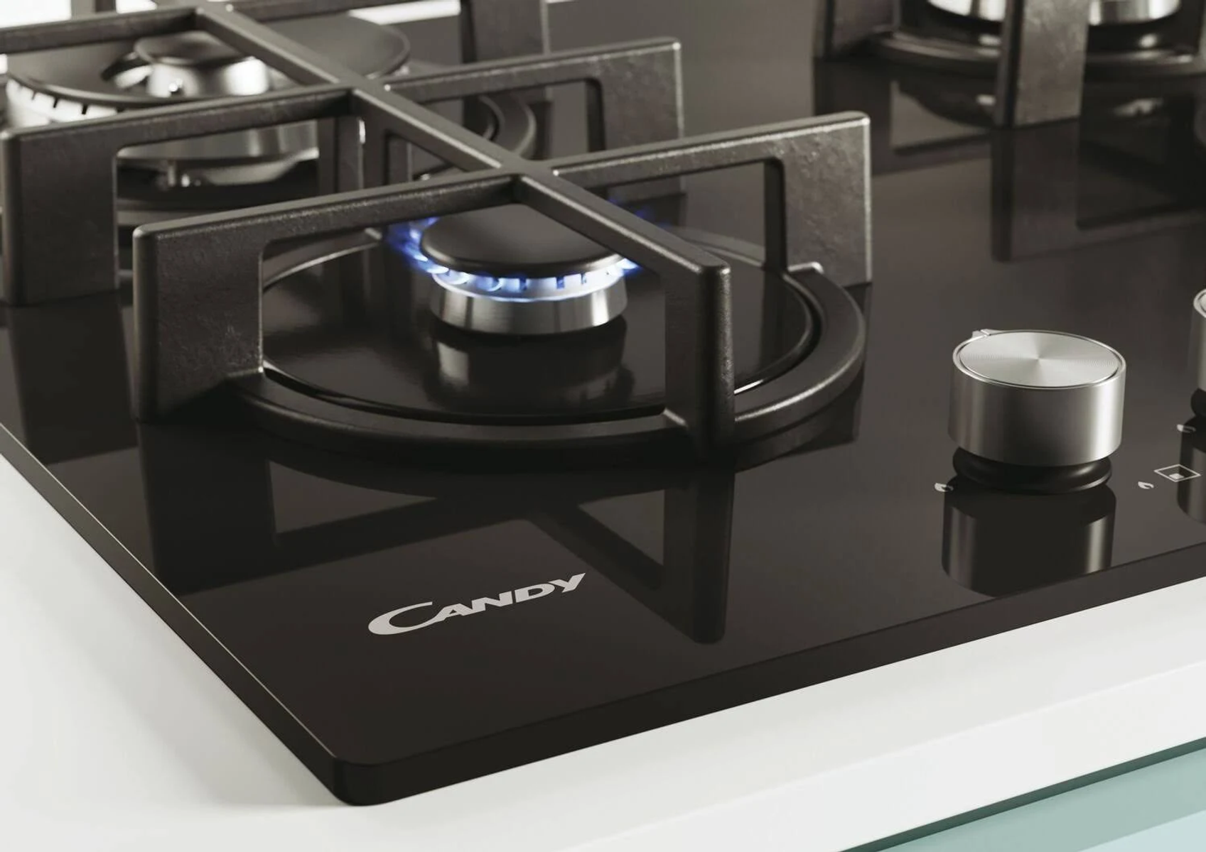 Zbliżenie czarnej płyty grzewczej z niebieskim płomieniem i logo Candy.