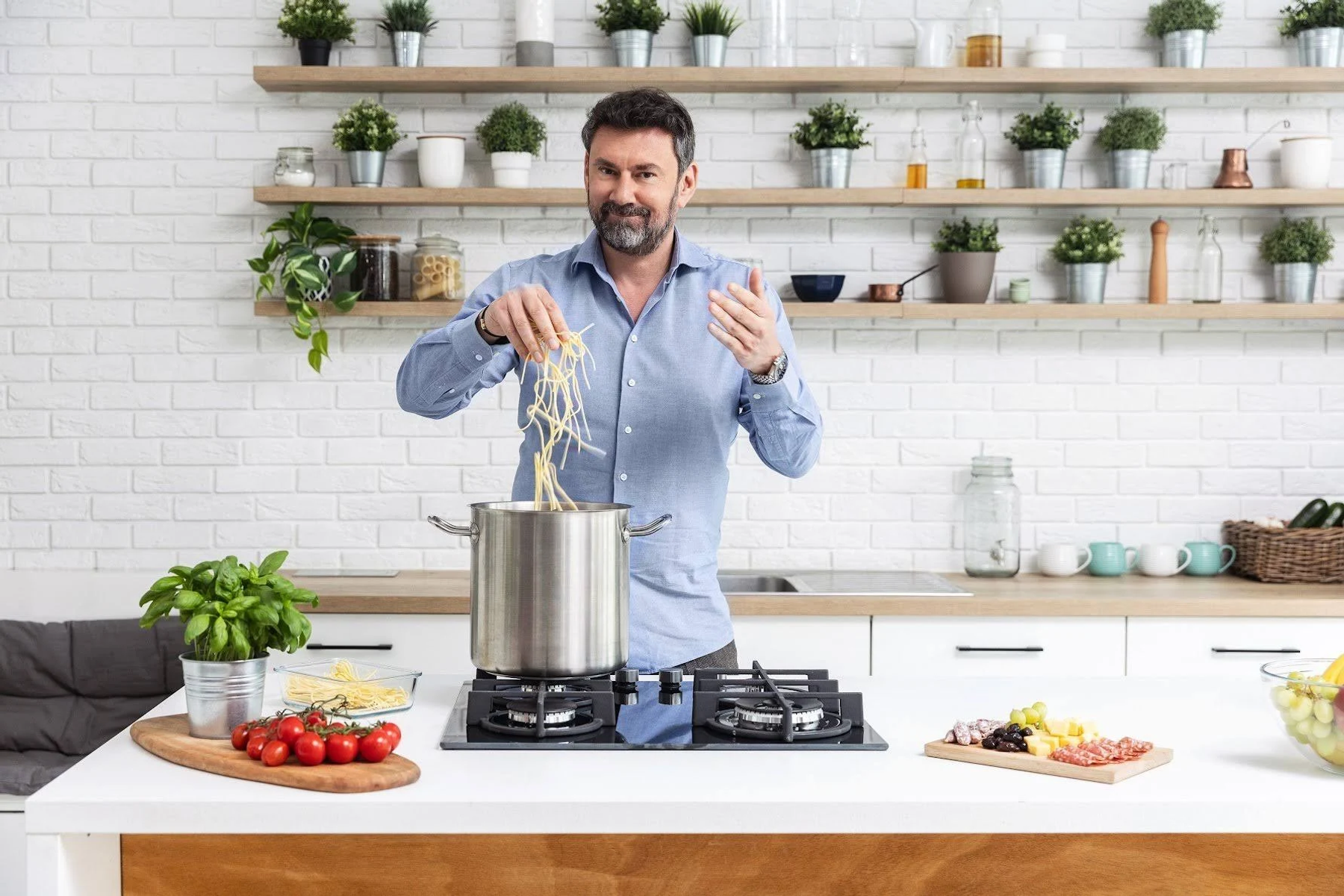 Mężczyzna dodaje makaron do garnka na płycie grzejnej. Otoczenie kuchni, widoczne składniki.