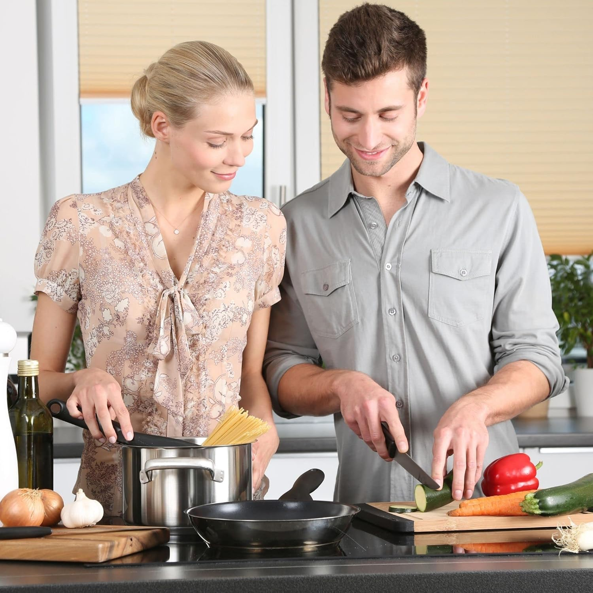 Coppia in cucina; donna guarda la pasta, uomo taglia zucchina.