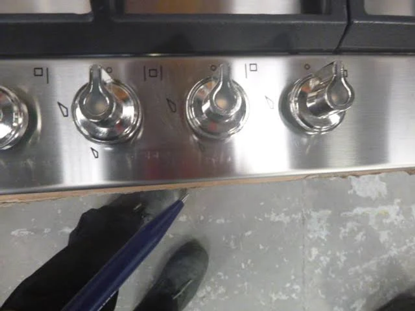 Placa de gas negra con cuatro quemadores sobre encimera blanca. Ambiente de cocina con armarios azul claro.