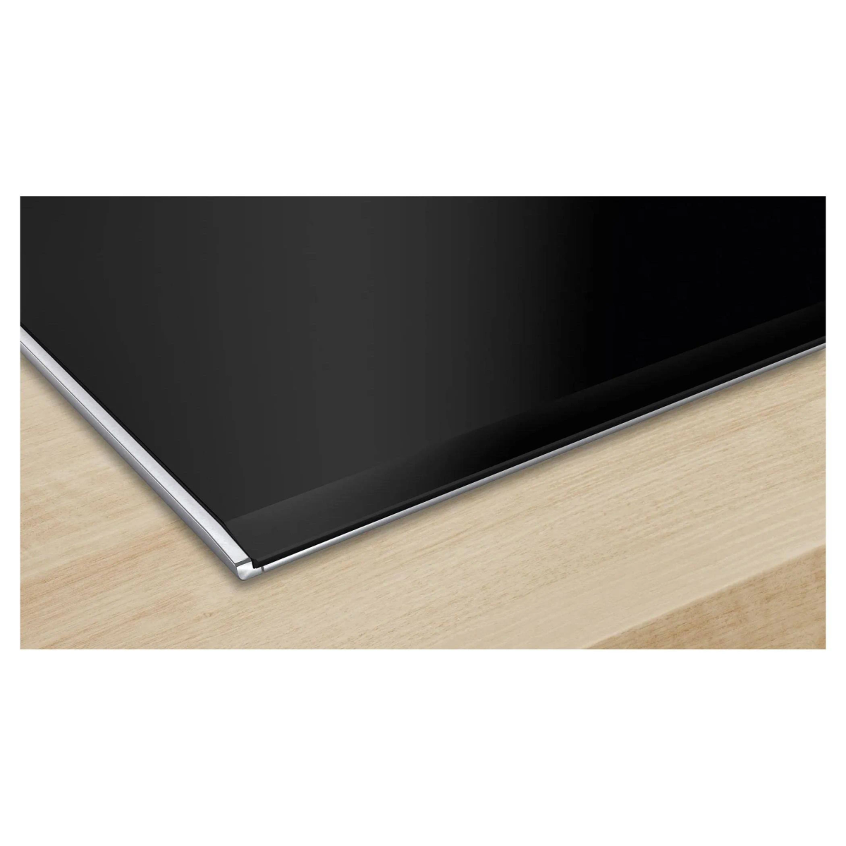 Primer plano de una placa de inducción negra con borde metálico, sobre una superficie de madera.