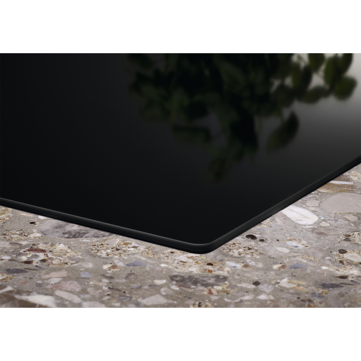 Czarna szklana płyta grzewcza, błyszcząca powierzchnia, widok z rogu, na nakrapianym blacie.