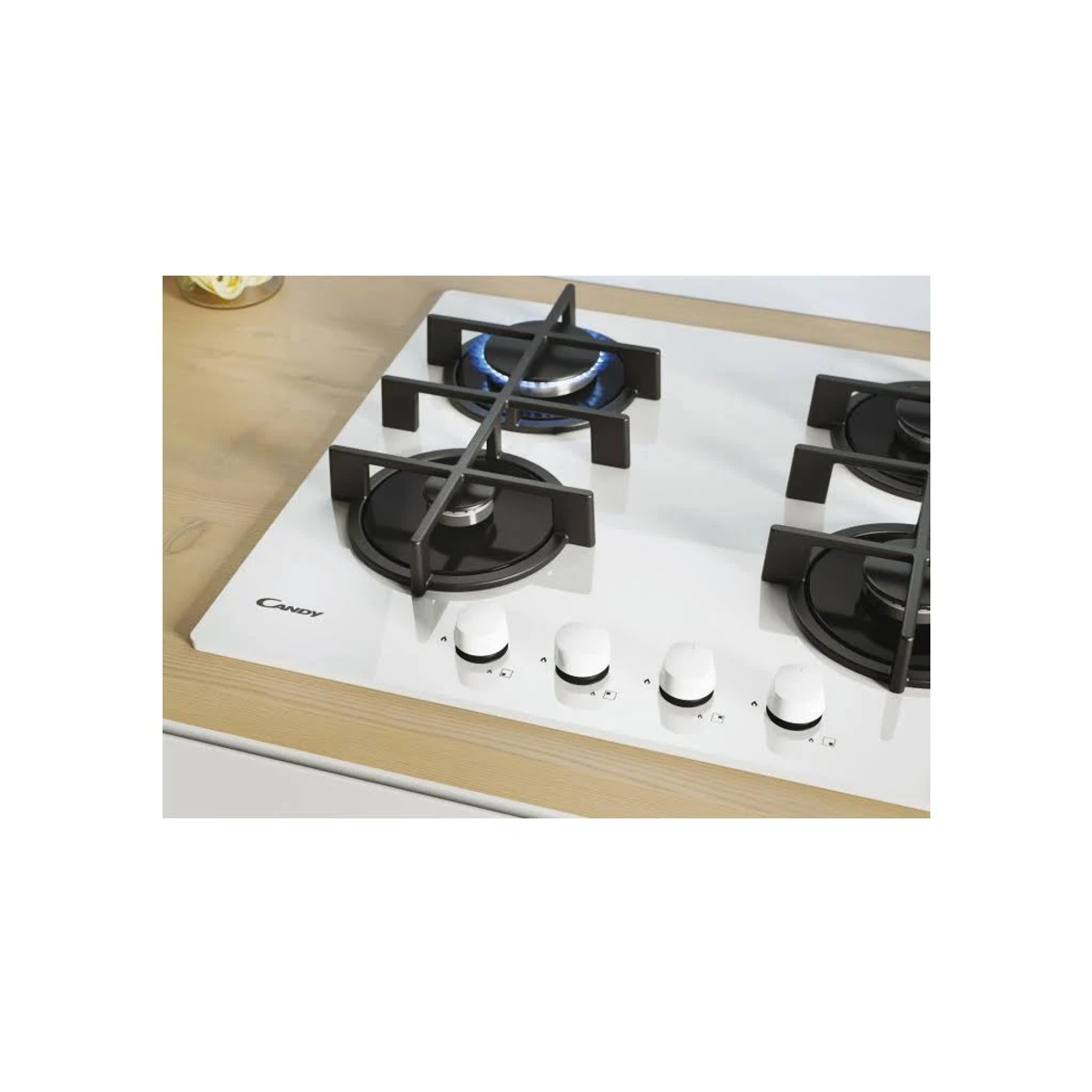 Biała płyta gazowa Candy z czterema palnikami i czarnymi rusztami. Jeden palnik z niebieskim płomieniem.