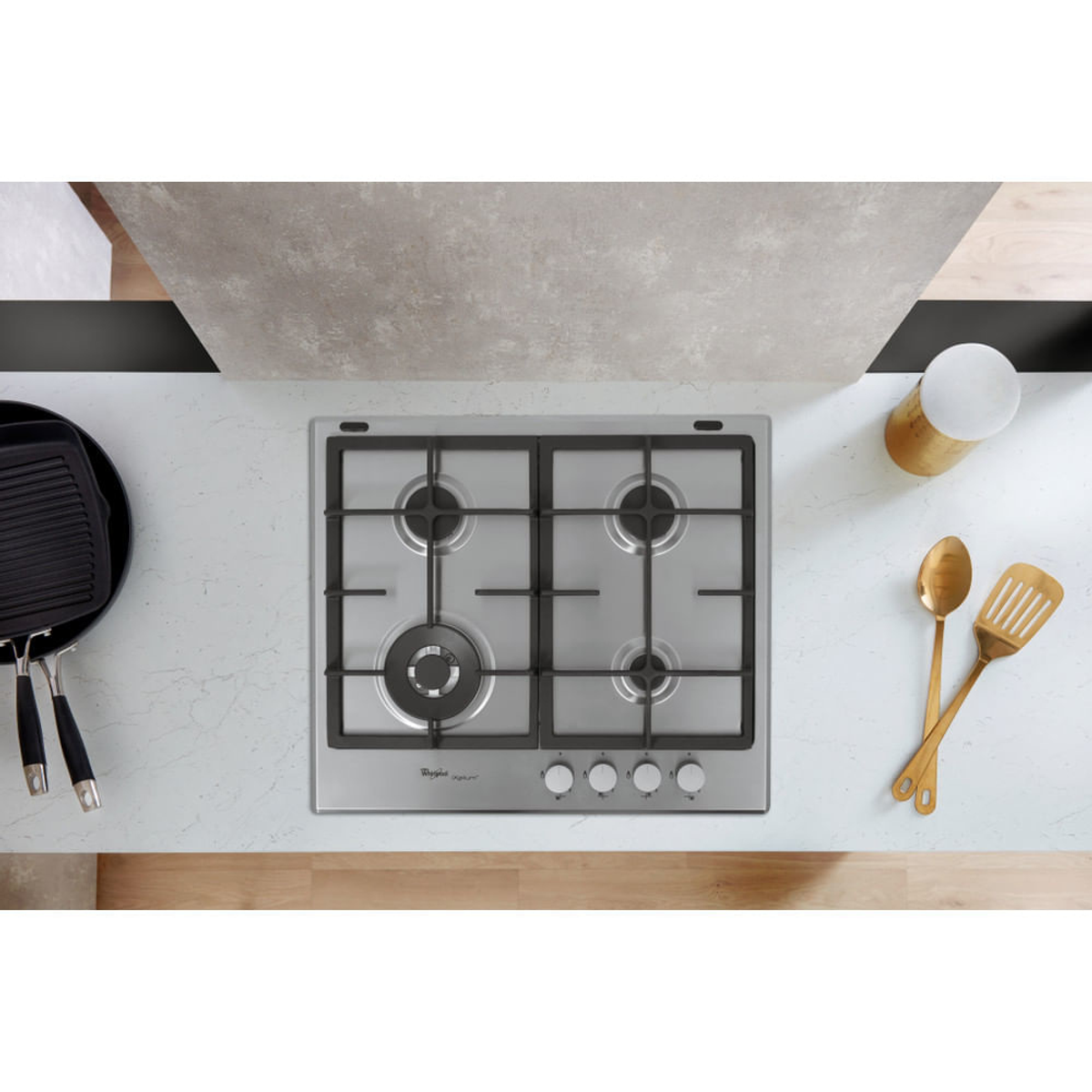 Widok z góry na kuchenkę gazową z czterema palnikami. Złote przybory i czarna patelnia grillowa.
