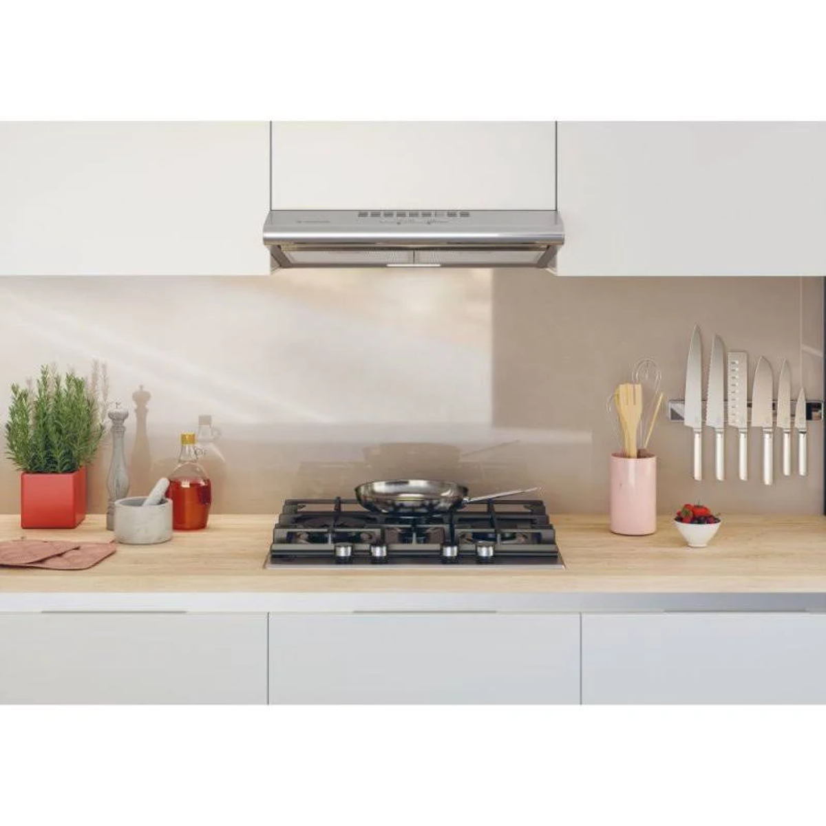 Scena di cucina con piano cottura a gas, cappa aspirante e utensili da cucina su un piano di lavoro.