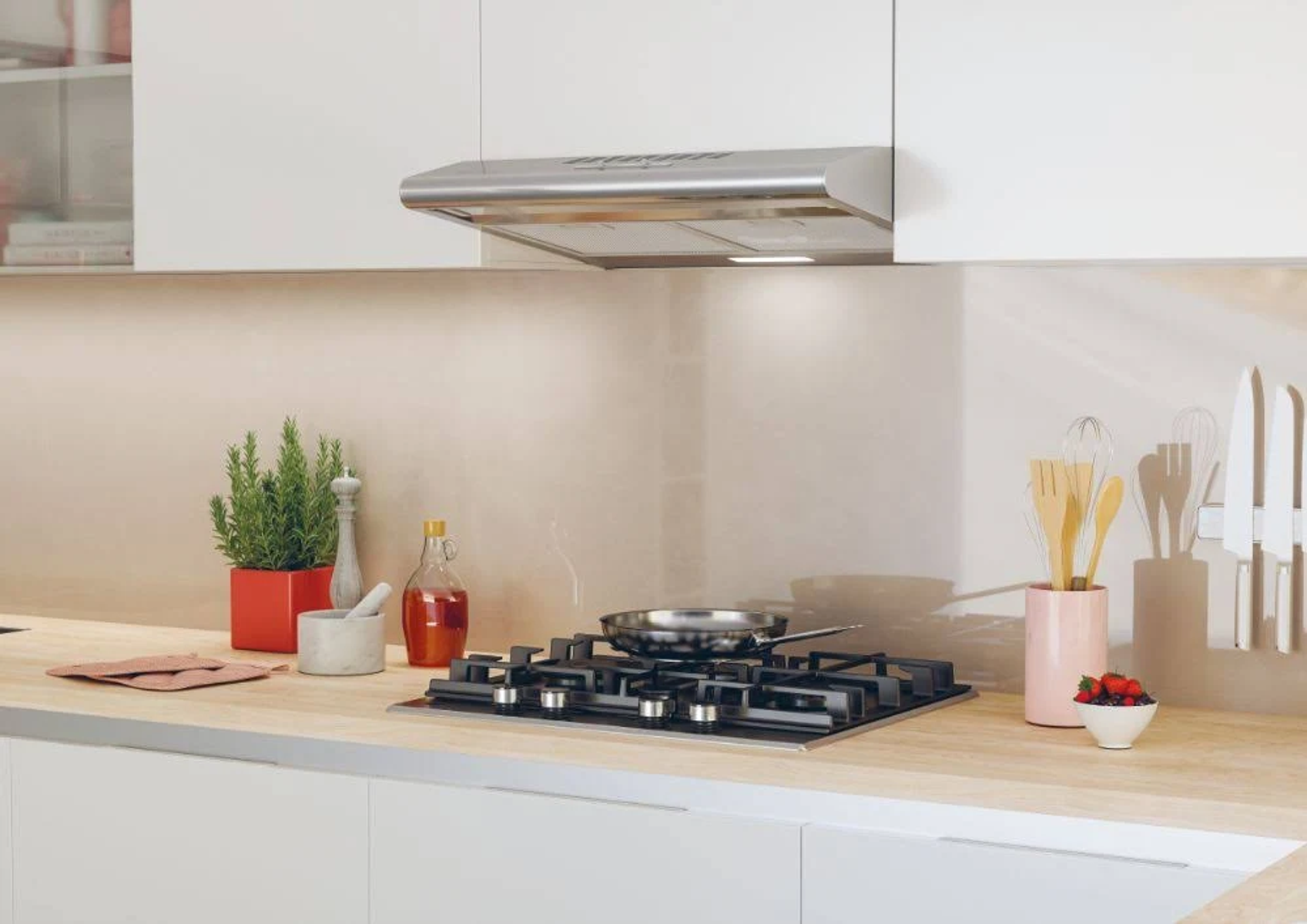 Scena di cucina con piano cottura, cappa e vari oggetti sul piano di lavoro.