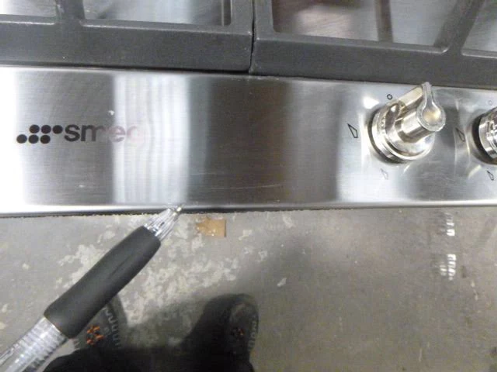 Primer plano de una placa Smeg de acero inoxidable con un bolígrafo apuntando a la superficie.