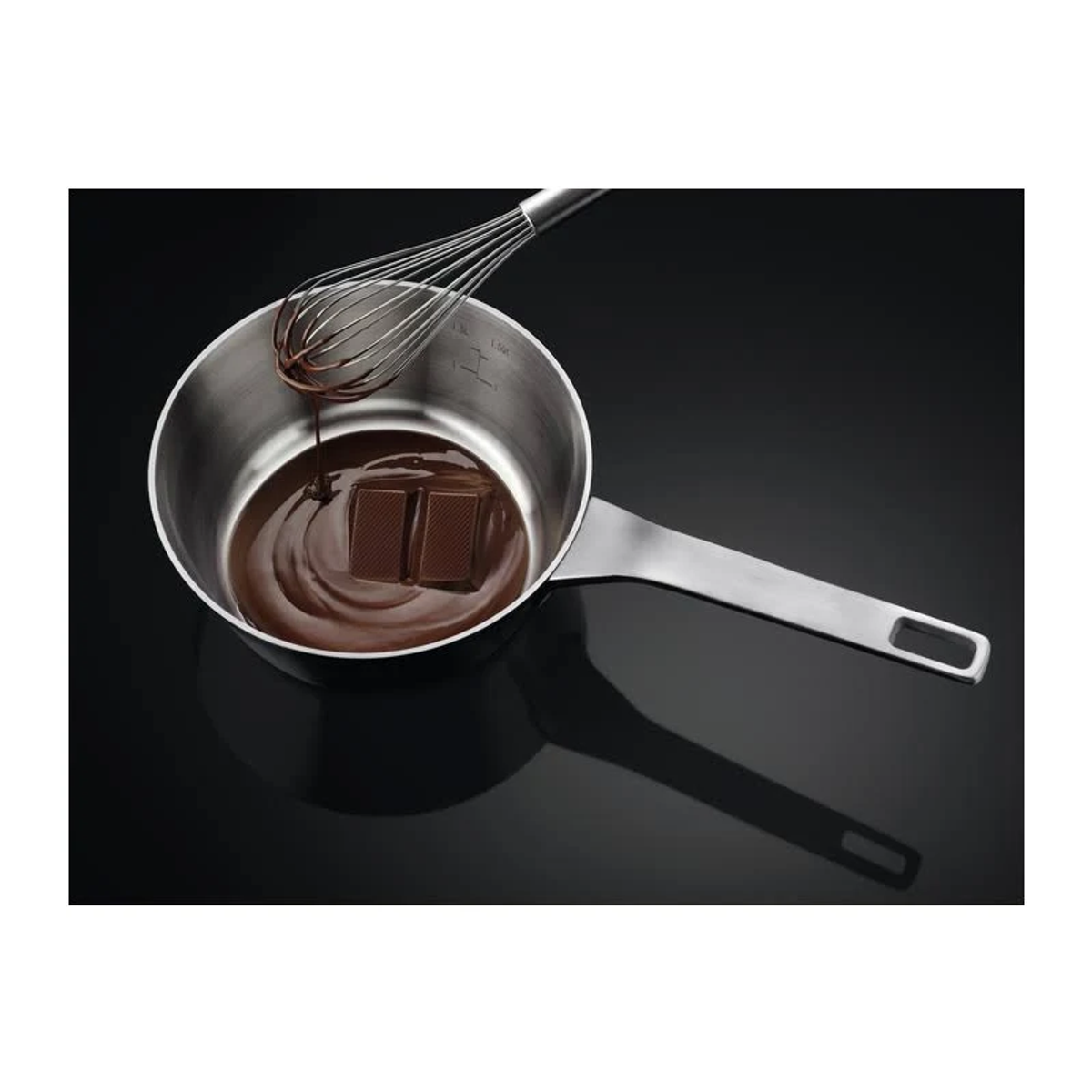 Rondel z roztopioną czekoladą i trzepaczką na czarnej powierzchni.