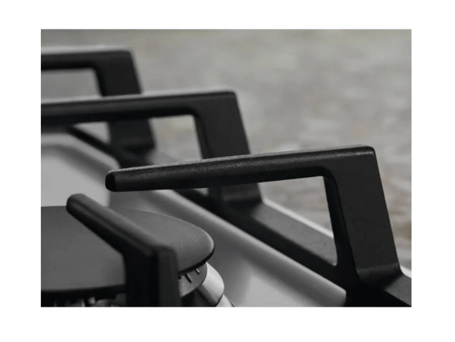 Zbliżenie na płytę gazową z czarnymi kratkami i wspornikami palników.