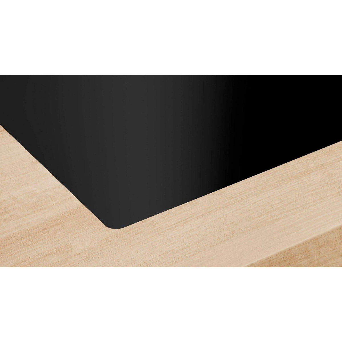 Un piano cottura nero inserito in un piano di lavoro in legno chiaro. Primo piano.