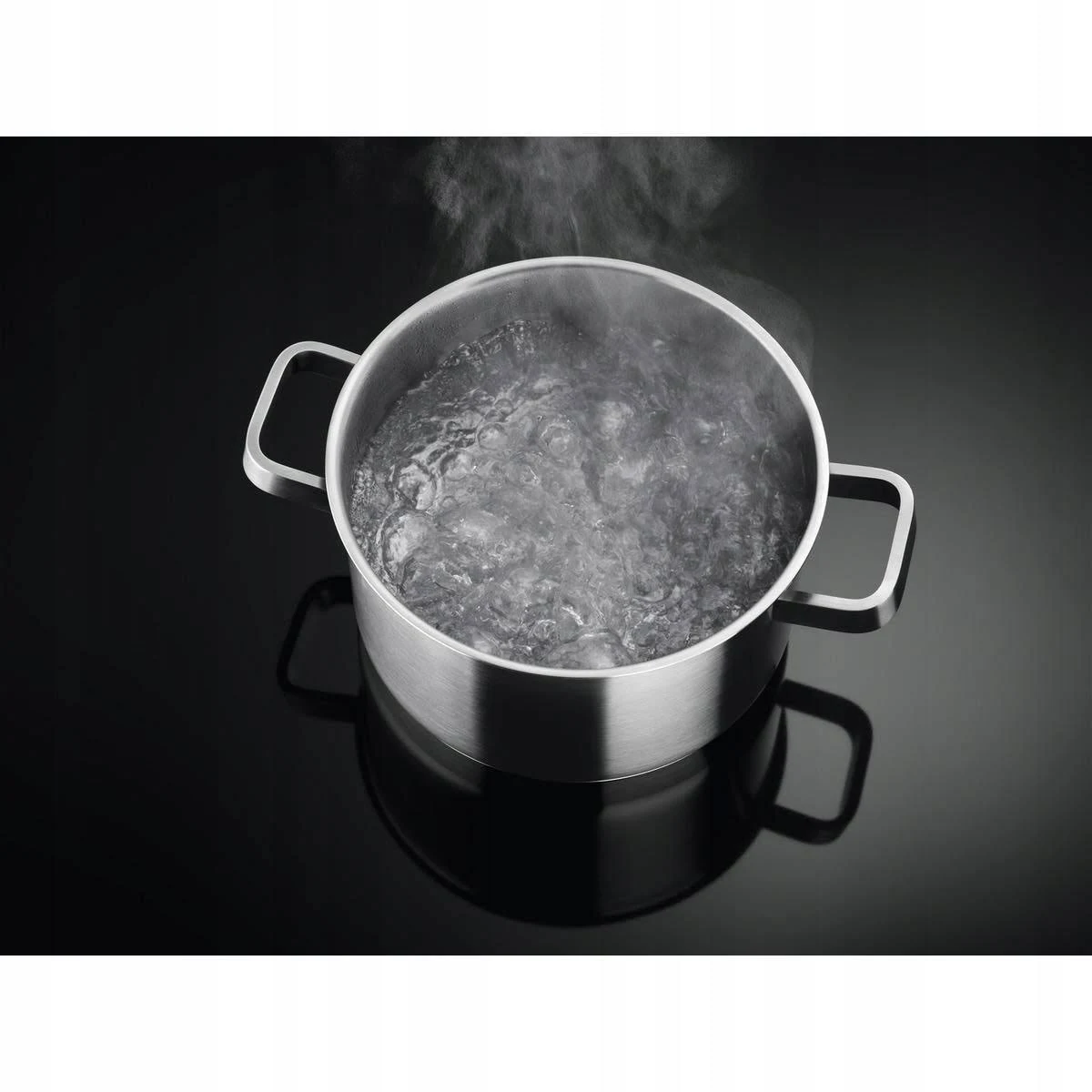 Una pentola in acciaio inox con acqua bollente su un piano cottura nero. Il vapore sale.