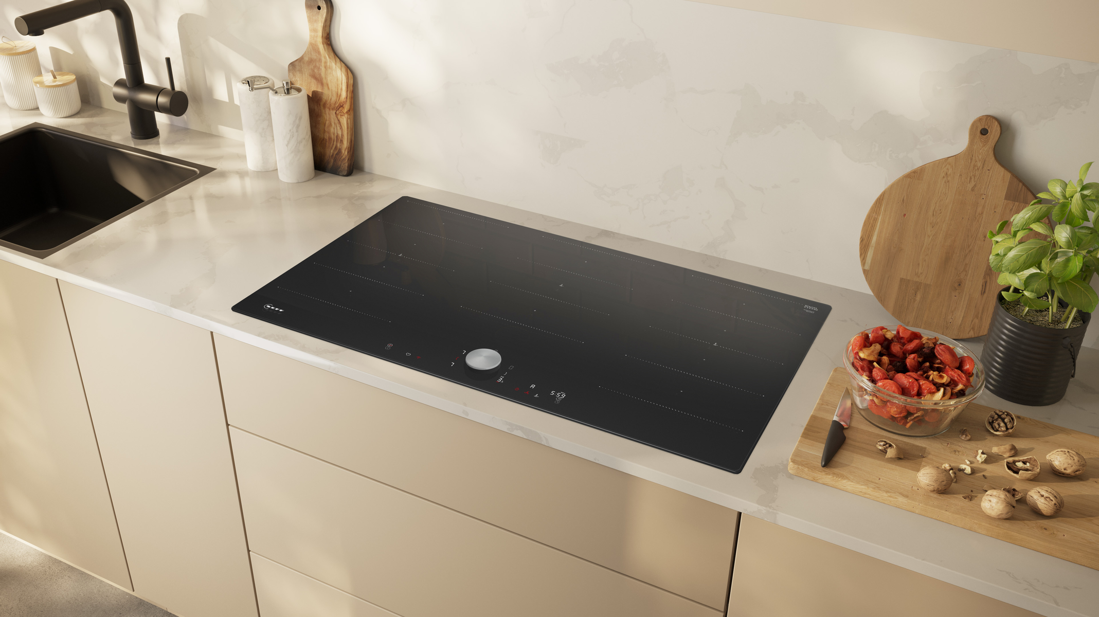 Cucina moderna con un piano cottura nero su un piano di lavoro bianco. Frutta, taglieri e piante sul piano di lavoro.