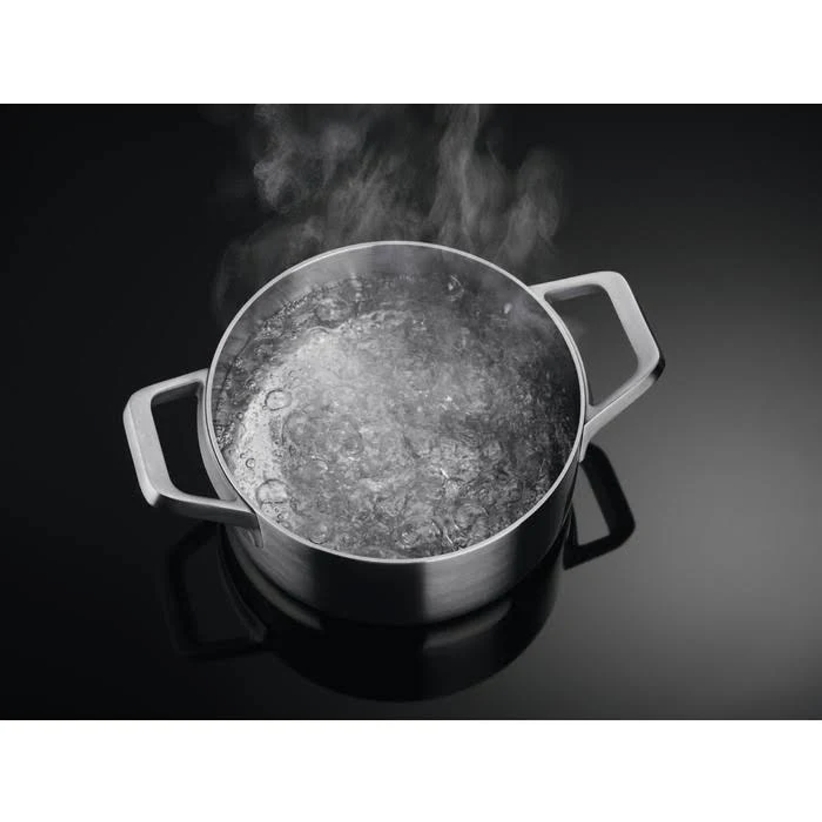 Una pentola d'argento con acqua bollente su un piano cottura nero. Il vapore sale dall'acqua.