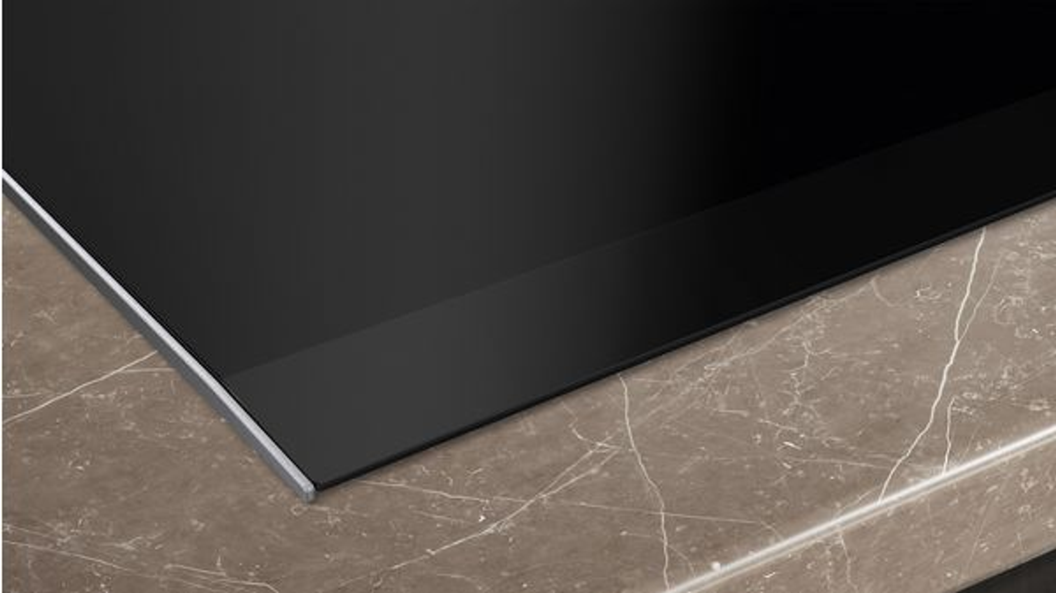 Zbliżenie czarnej płyty grzewczej na brązowym blacie z efektem marmuru i srebrną krawędzią.