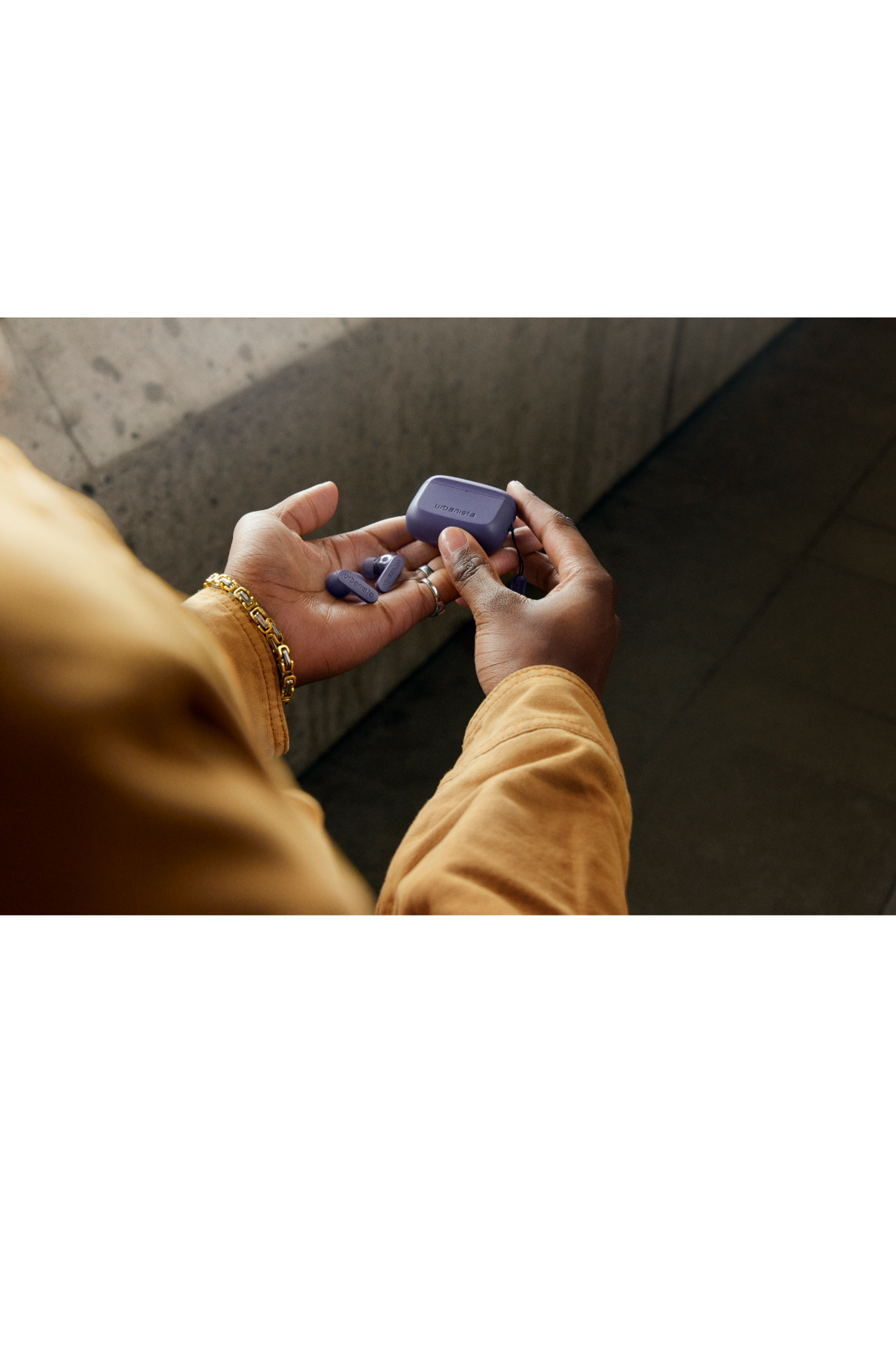 Hände halten violette kabellose Ohrhörer und Ladecase, beige Kleidung.