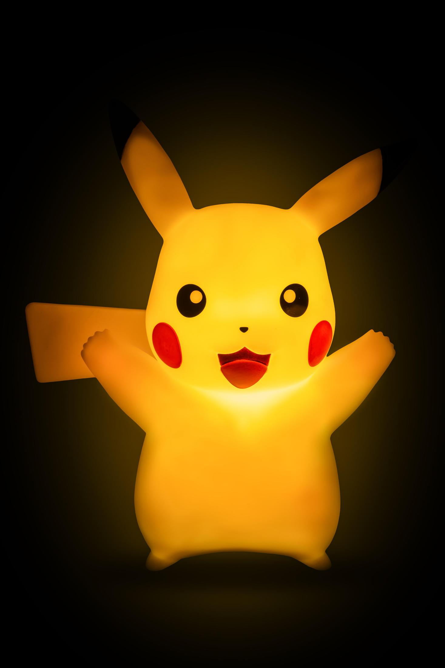 Una lampada di Pikachu, gialla con guance rosse, sorridente con le braccia tese, su sfondo nero.