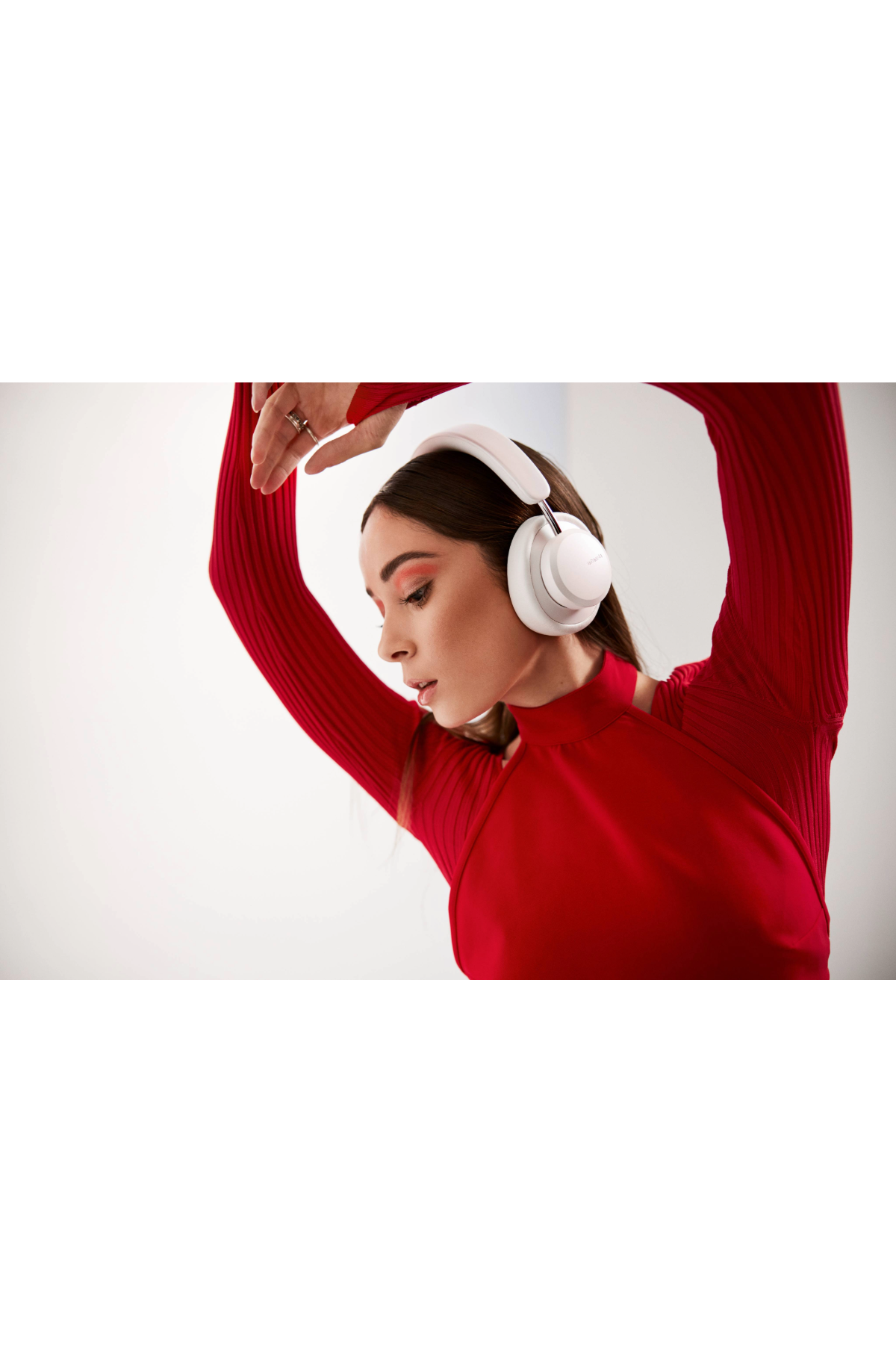 Kobieta w białych słuchawkach i czerwonym topie pozuje z podniesionymi ramionami.
