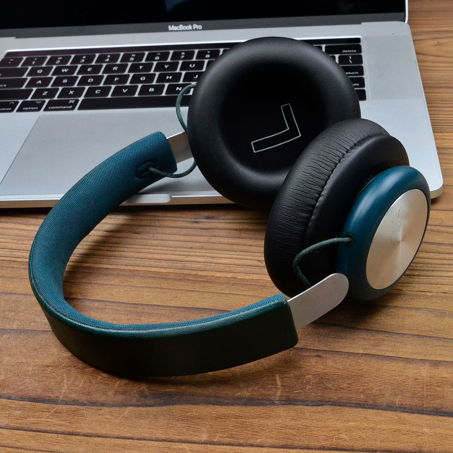 Słuchawki na laptopie. Są czarne i morskie. Laptop jest na drewnianym stole.